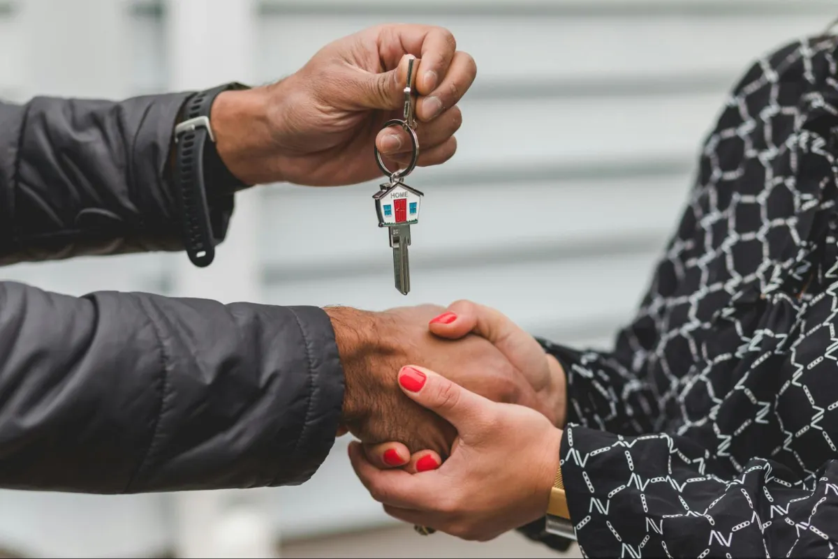 A person handing over house keys to a new owner with a handshake.
