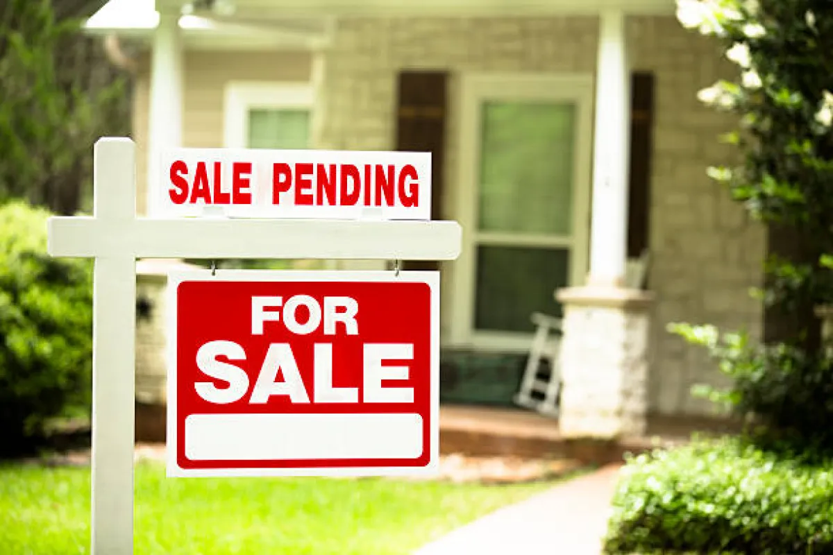 A 'For Sale' sign with 'Sale Pending' text in front of a house.